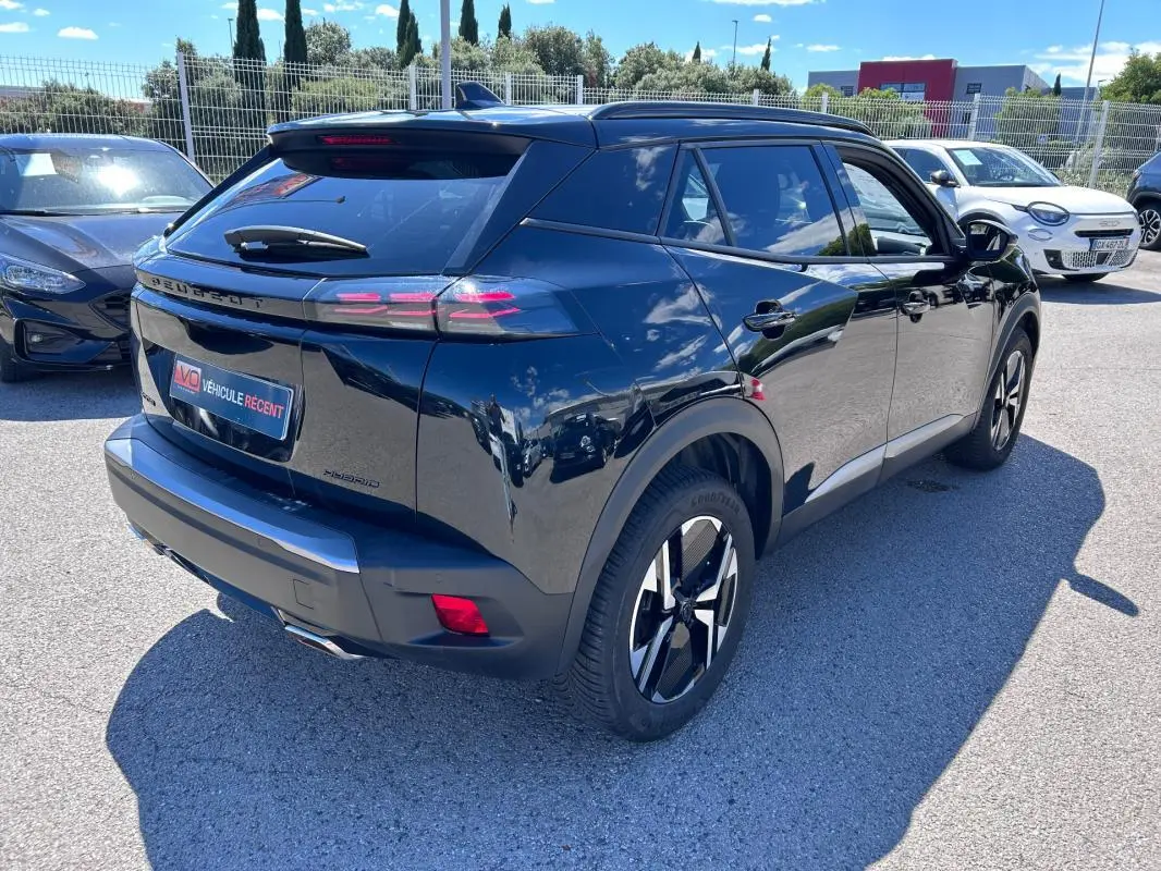 Vue 3/4 arrière droite d’un Peugeot 2008 Hybrid noir avec barres de toit et jantes alliage 17 pouces brillantes.