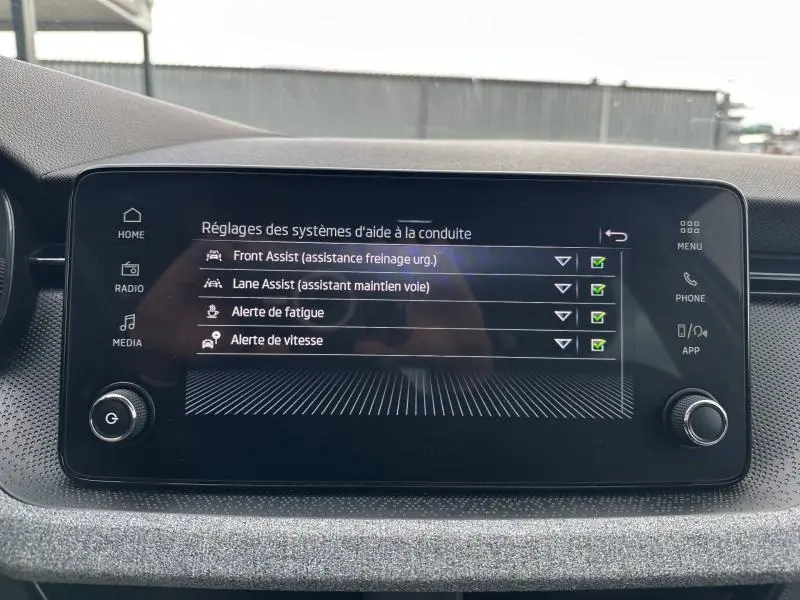 Écran tactile central de la Skoda Scala blanc, affichant les réglages des aides à la conduite en intérieur.