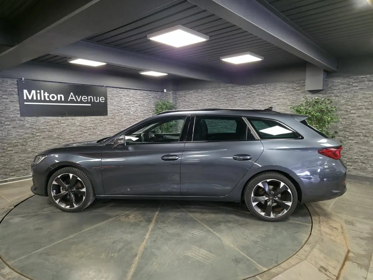Vue de profil côté gauche d'une CUPRA Leon Sportstourer gris magnétique avec jantes alliage 18 pouces dans un showroom.