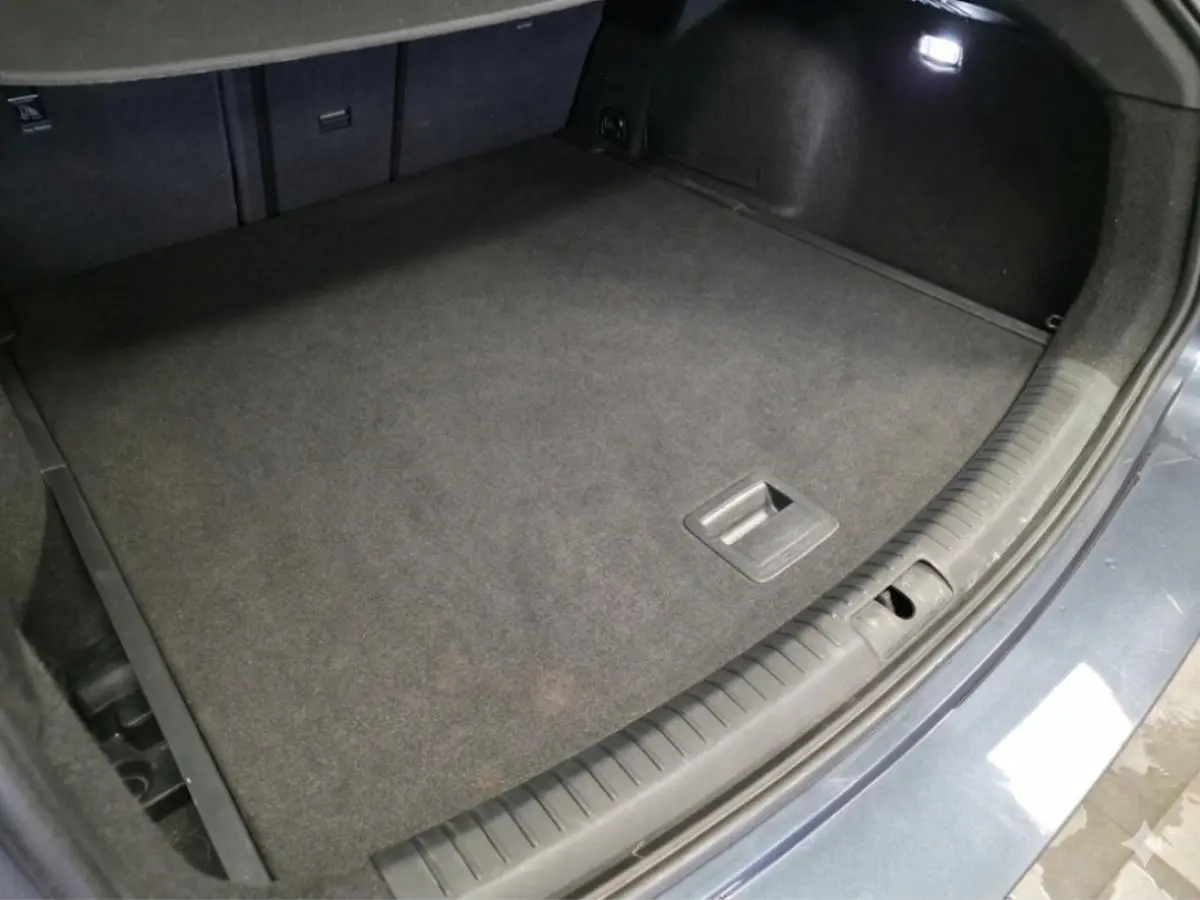Coffre ouvert vu de dessus du CUPRA Leon Sportstourer gris, avec tapis de sol noir et éclairage intérieur.