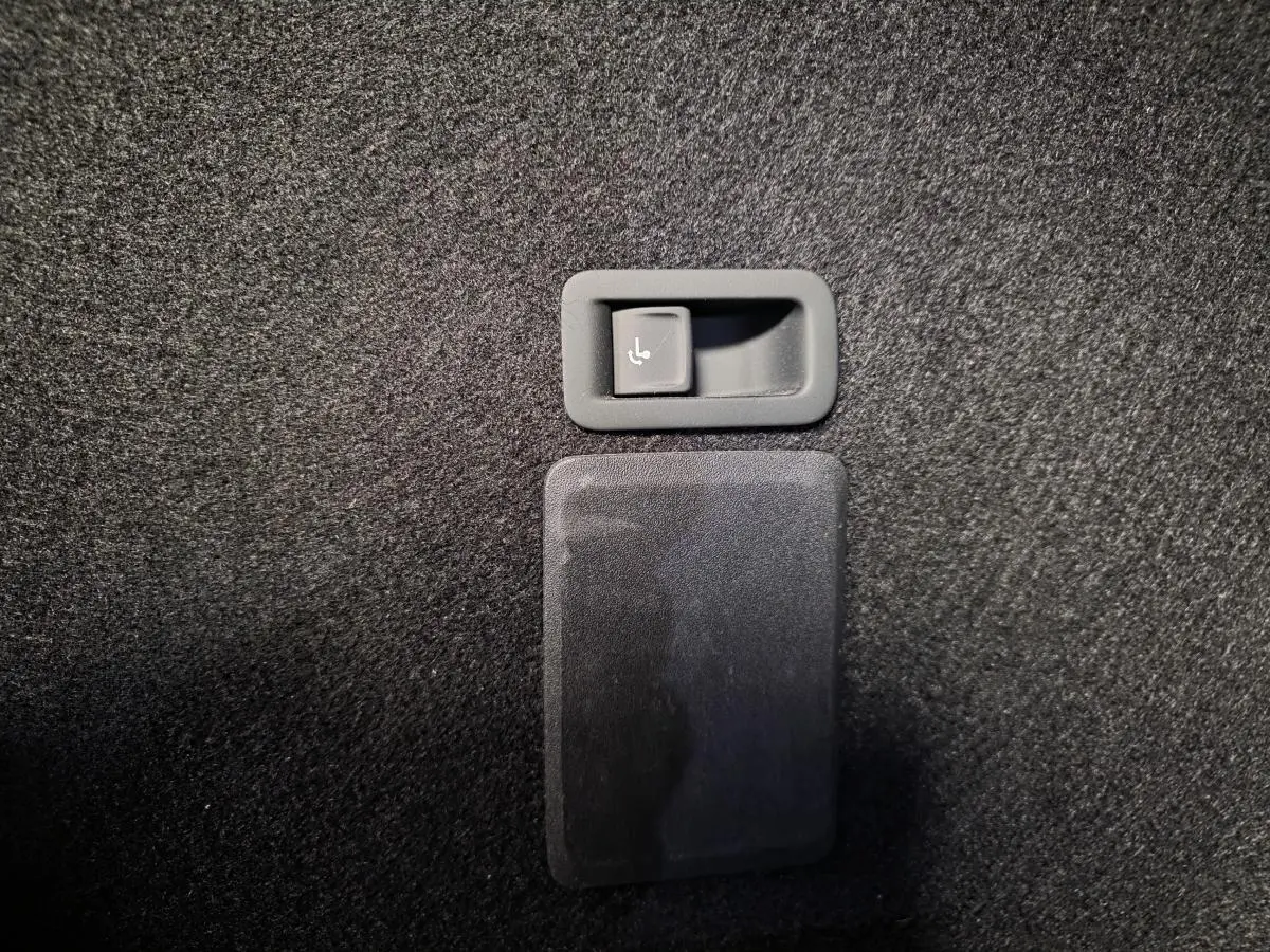 Détail du bouton de rabattement électrique des sièges arrière sur la moquette noire du coffre du CUPRA Leon Sportstourer gris.