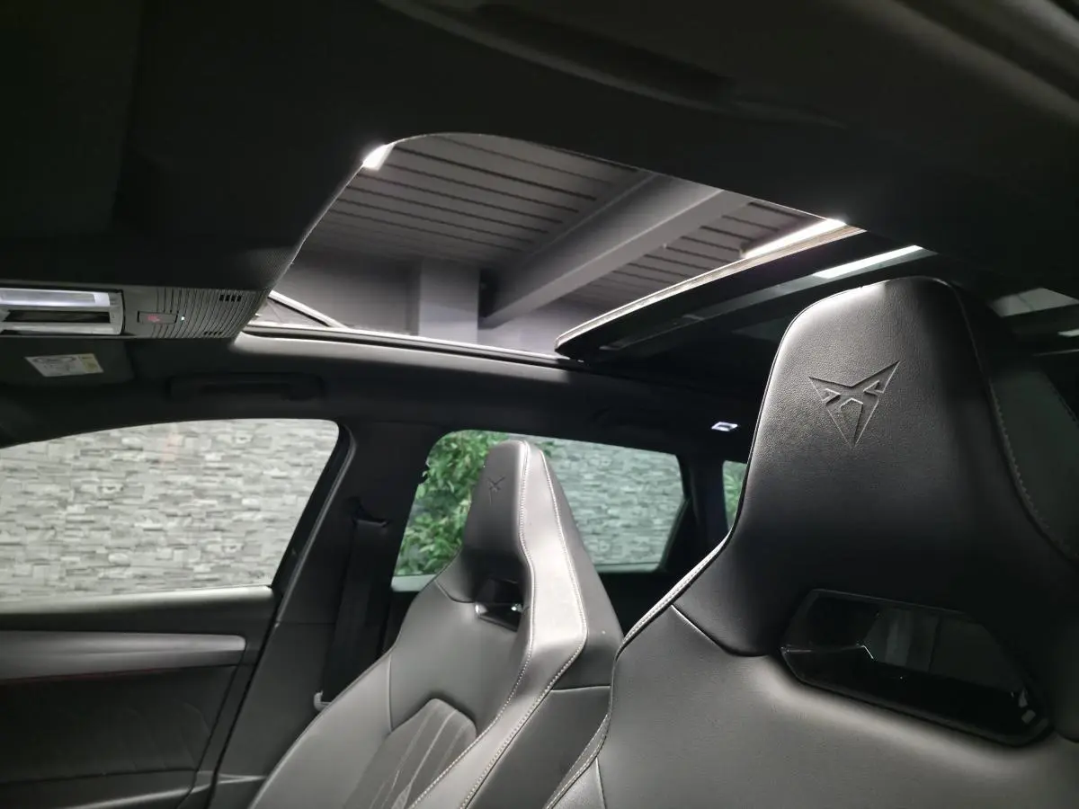 Vue intérieure montrant les sièges baquets noirs avec logo Cupra et le toit ouvrant panoramique ouvert.