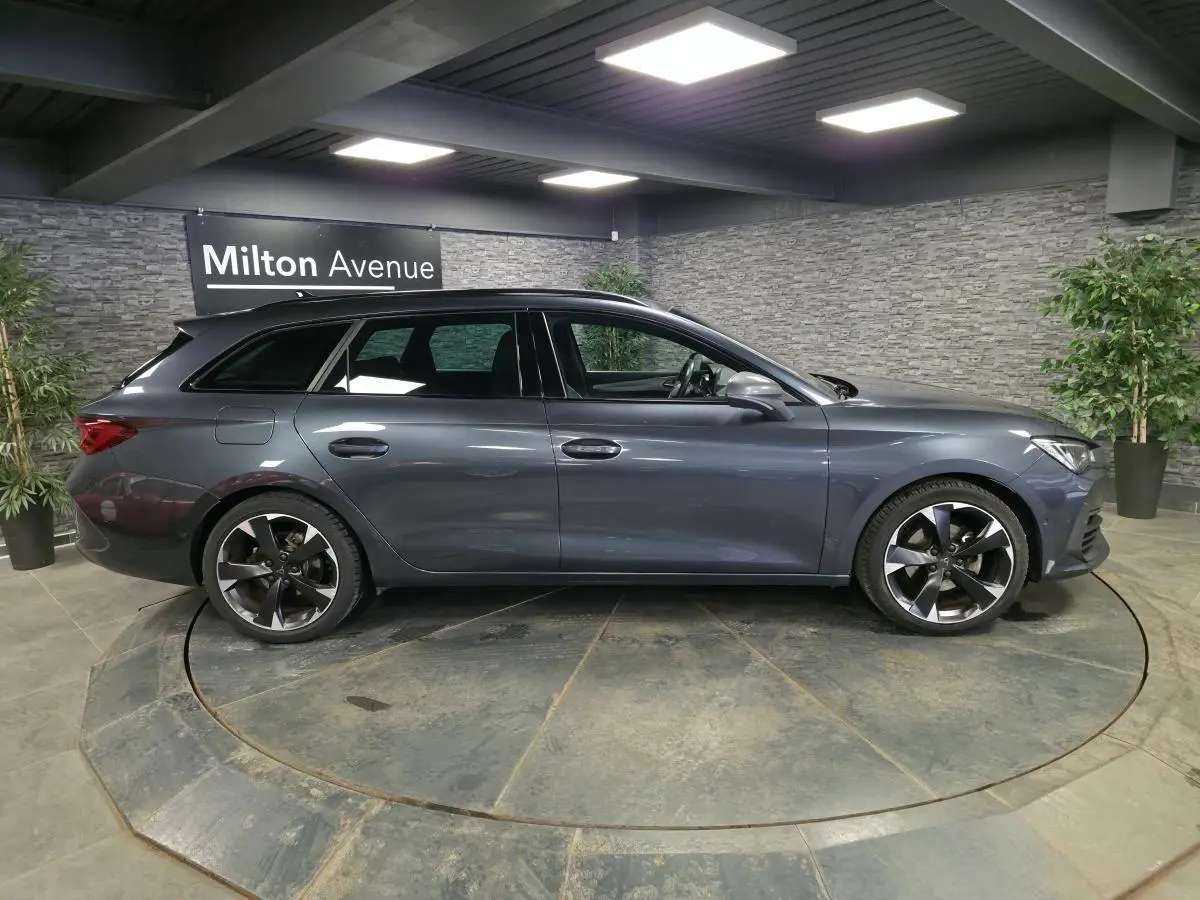 Profil droit d'une CUPRA Leon Sportstourer gris magnétique 2023 en intérieur avec jantes alliage 18 pouces.