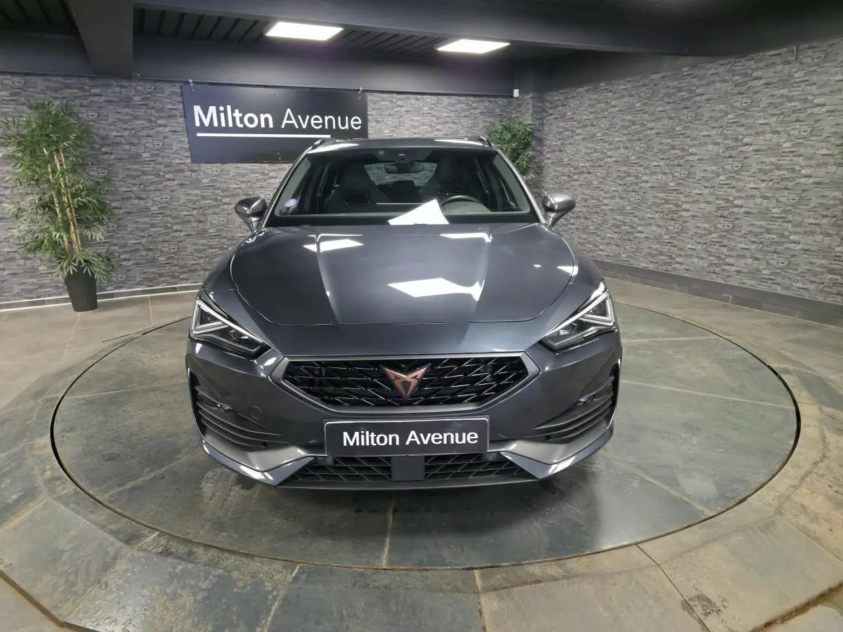Vue avant d'une CUPRA Leon Sportstourer gris magnétique, avec calandre noire et logo cuivre, en intérieur showroom.