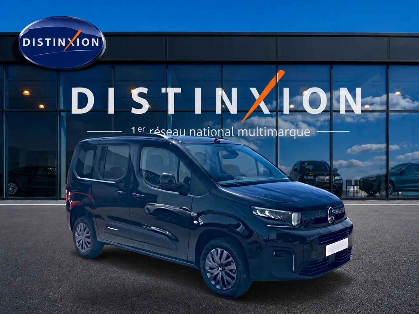 Vue 3/4 avant droite du Citroën Berlingo noir, avec barres de toit et jantes alu, devant une vitrine Distinxion.