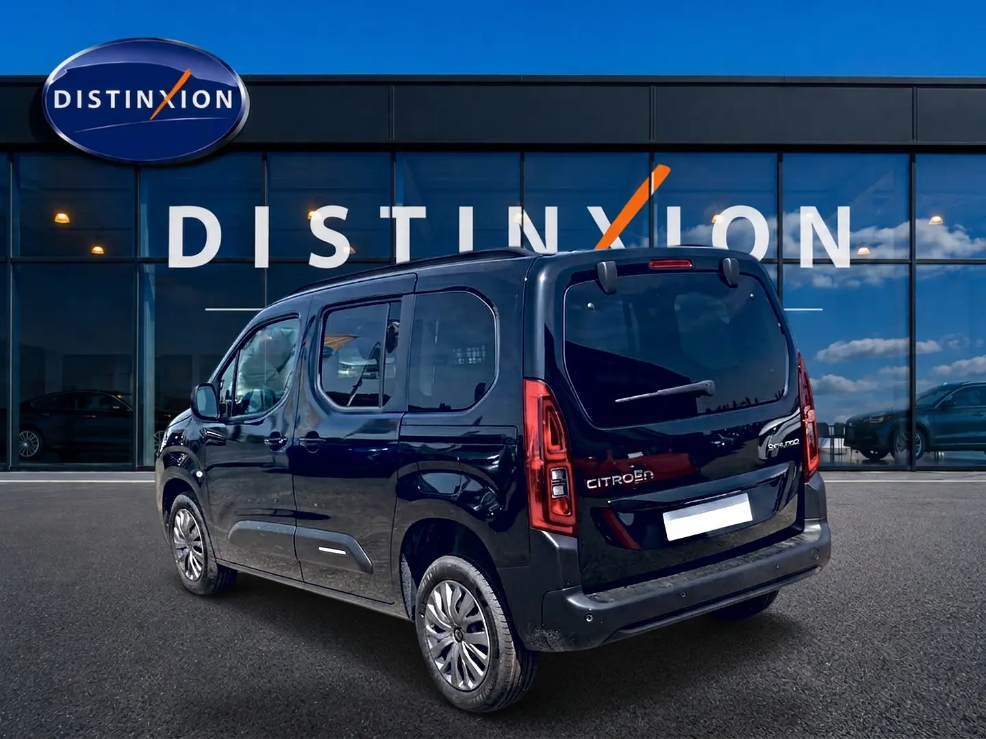 Vue 3/4 arrière droite du Citroën Berlingo noir avec barres de toit et vitres arrière teintées, devant un bâtiment Distinxion.