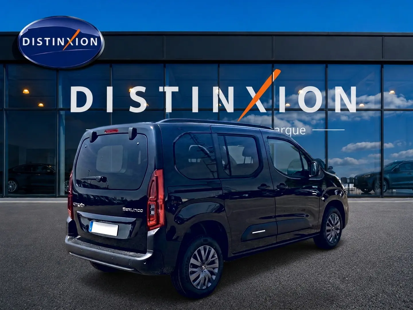 Vue 3/4 arrière droite d’un Citroën Berlingo noir 2026 avec barres de toit et vitres teintées, devant un showroom Distinxion.