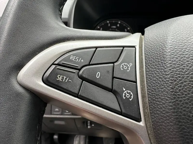 Gros plan sur les commandes de régulateur de vitesse au volant côté gauche du Dacia Jogger 2025, intérieur noir.
