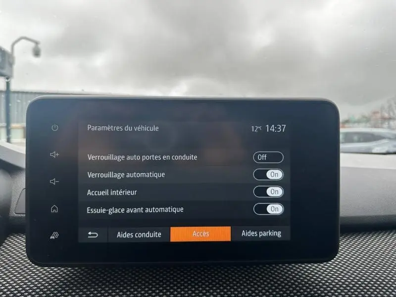 Écran tactile du tableau de bord du Dacia Jogger affichant les paramètres d'accès et de verrouillage, avec fond extérieur nuageux.