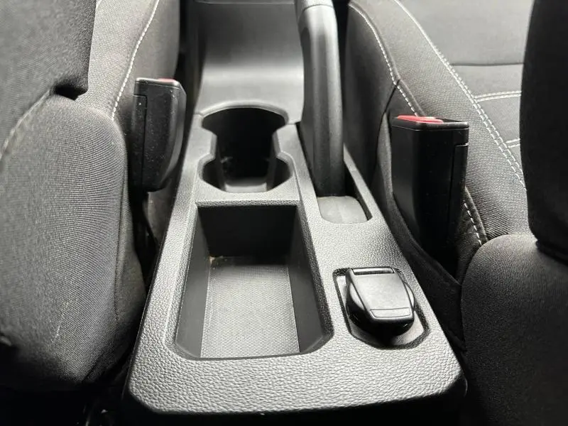 Gros plan sur la console centrale noire entre les sièges avant du Dacia Jogger 2025, avec porte-gobelets et frein à main manuel.