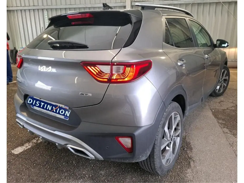 Vue 3/4 arrière droit d'un KIA STONIC gris météore 2024 avec feux allumés et finition GT Line visible en intérieur d'atelier.