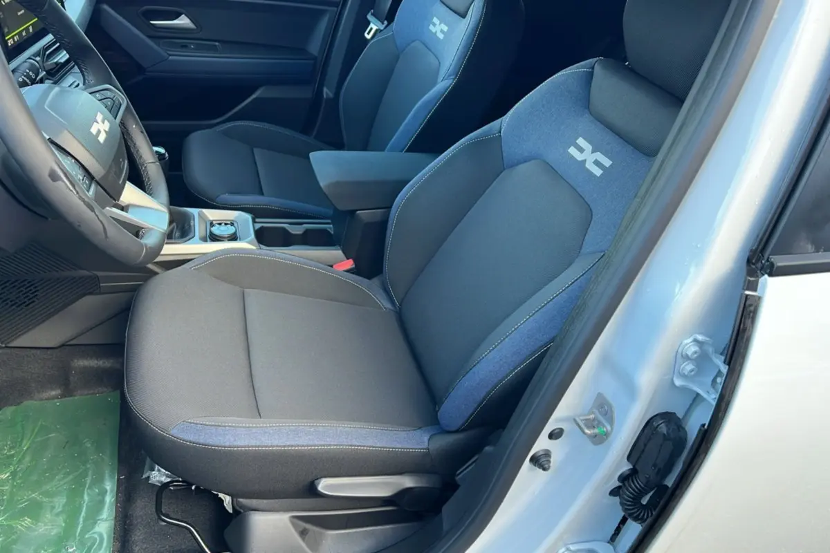 Vue intérieure côté conducteur du Dacia Duster 2026, sièges tissu noir et bleu avec accoudoir central.