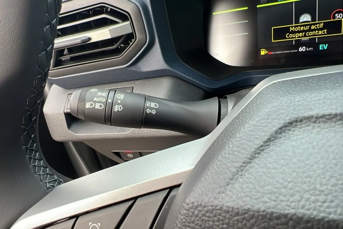 Détail du commodo d’éclairage à gauche du volant cuir dans le tableau de bord du Dacia Duster noir nacré 2026.