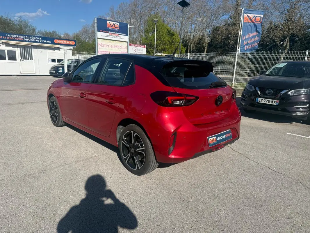 Vue 3/4 arrière droite d'une Opel Corsa rouge 2025 avec toit noir et jantes alliage noires, stationnée en extérieur.
