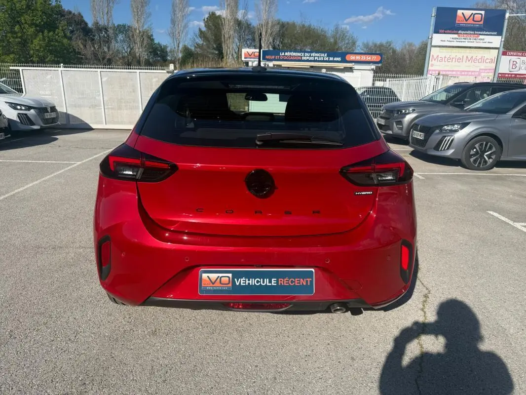 Vue arrière d'une Opel Corsa rouge 2025 hybride, avec feux arrière modernes et badge "Hybrid" visible.