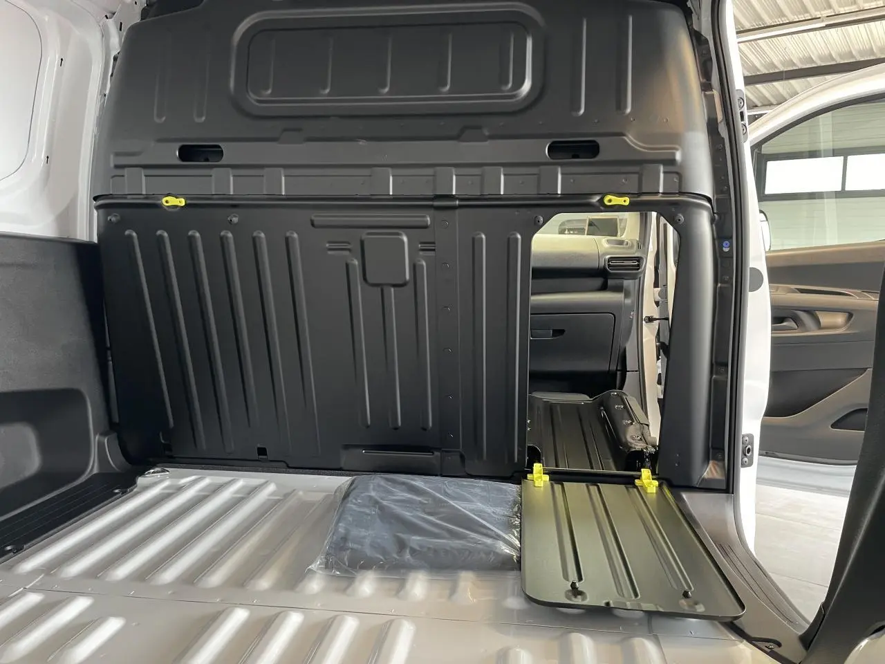 Vue intérieure du fourgon blanc Peugeot Partner 2026, montrant la cloison pleine fixe et la banquette passager rabattue avec tablette écritoire.