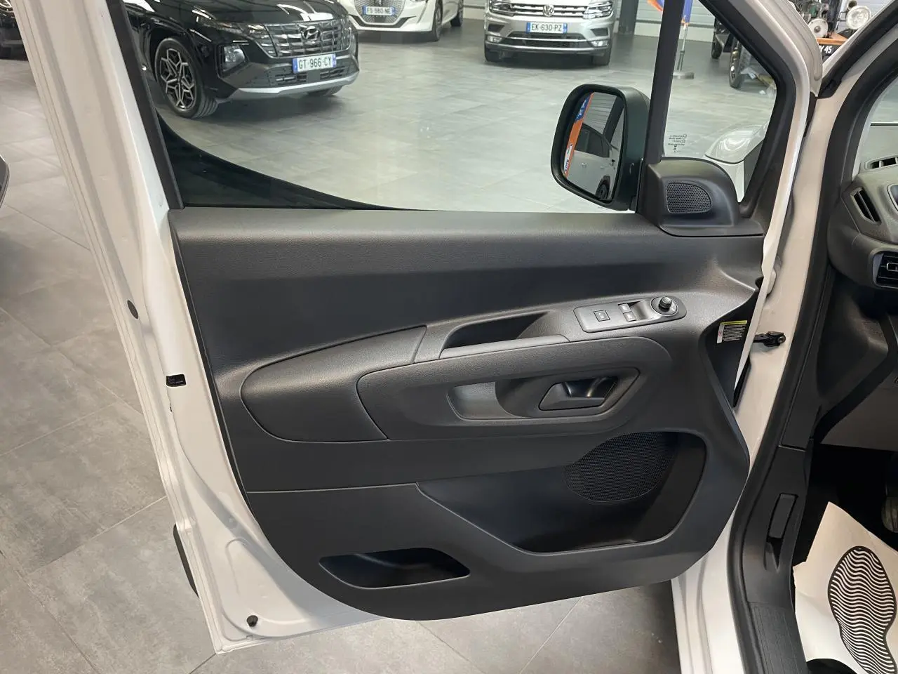 Vue rapprochée de la porte avant gauche blanche du Peugeot Partner 2026, avec commandes de vitres électriques et rétroviseur.