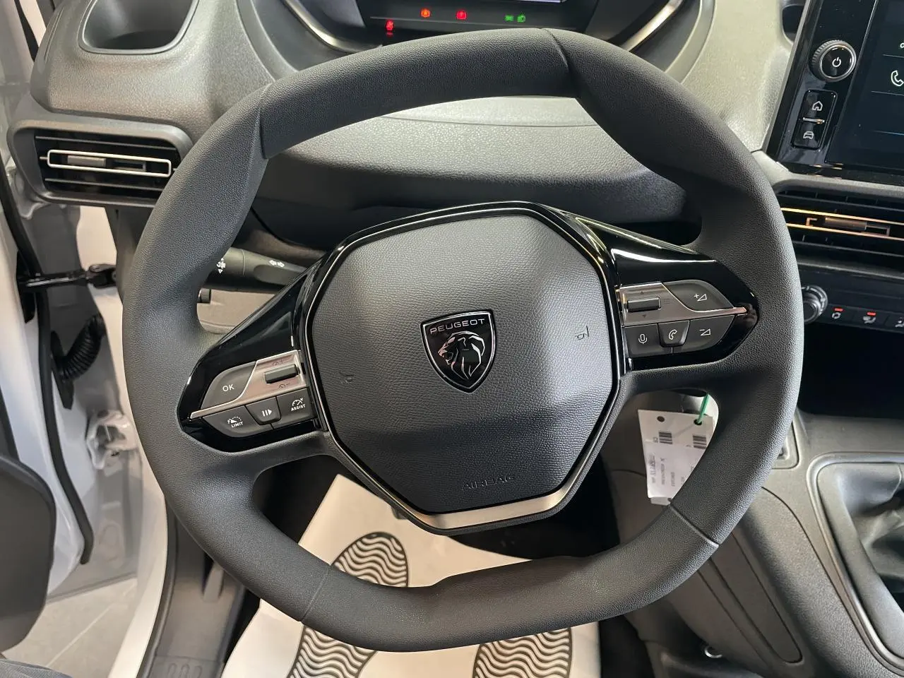 Vue rapprochée du volant noir de la Peugeot Partner 2026 avec commandes intégrées et tableau de bord partiel visible.