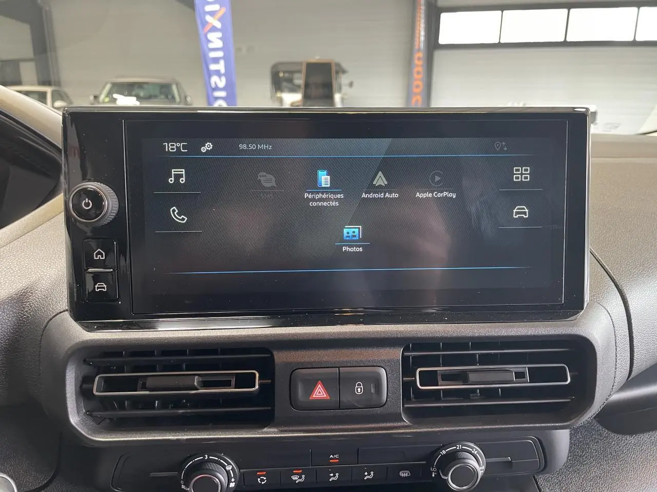 Écran tactile central du tableau de bord du Peugeot Partner blanc, vue frontale rapprochée avec commandes climatisation visibles.