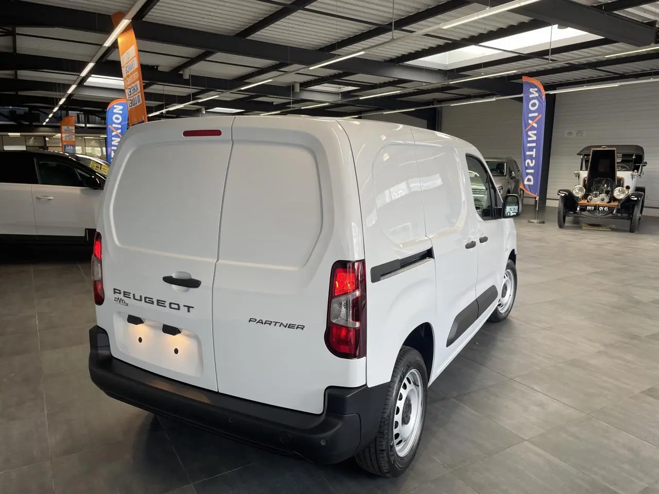 Vue 3/4 arrière droite du Peugeot Partner blanc utilitaire avec portes arrière battantes et jantes tôles grises.