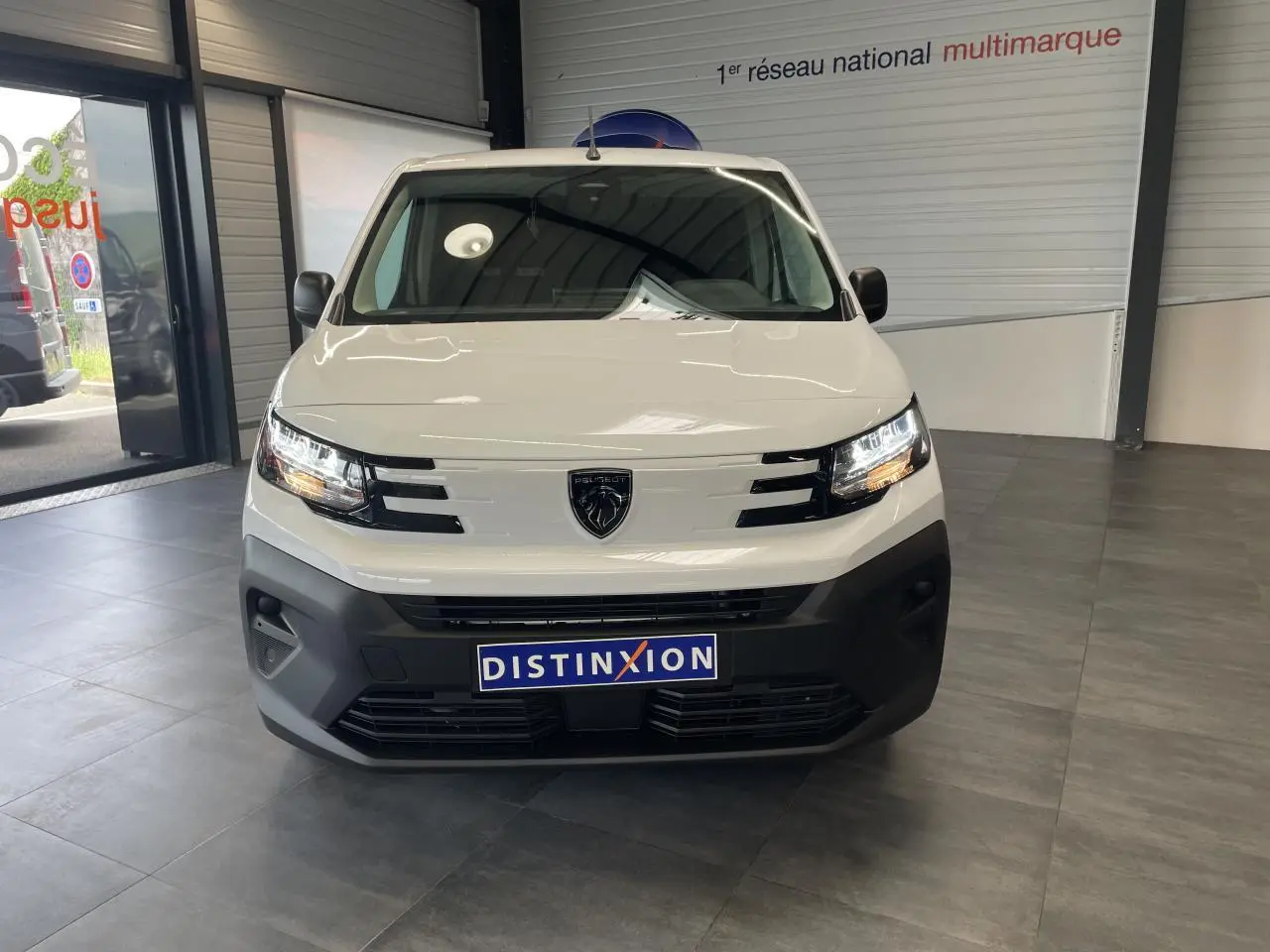 Vue avant d'un Peugeot Partner blanc 2026 avec calandre noire et logo lion au centre, en intérieur showroom.