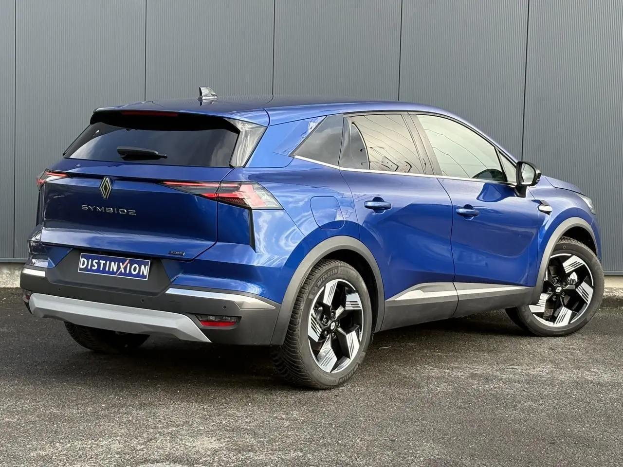 Vue 3/4 arrière droite d'un Renault Symbioz bleu Iron avec jantes 18 pouces et hayon mains libres.