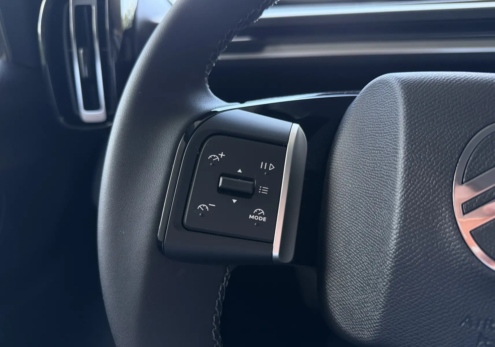Gros plan sur les commandes du régulateur de vitesse au volant noir d'une Citroën E-C3 113 MAX 2025 gris Mercury.