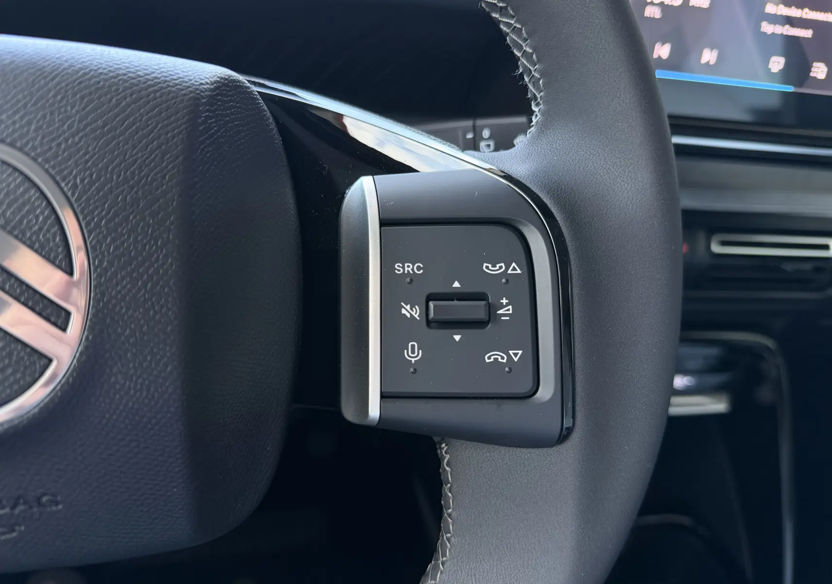 Gros plan sur les commandes multifonctions au volant cuir gris d’une Citroën C3 E-C3 113 MAX 2025, tableau de bord en arrière-plan.