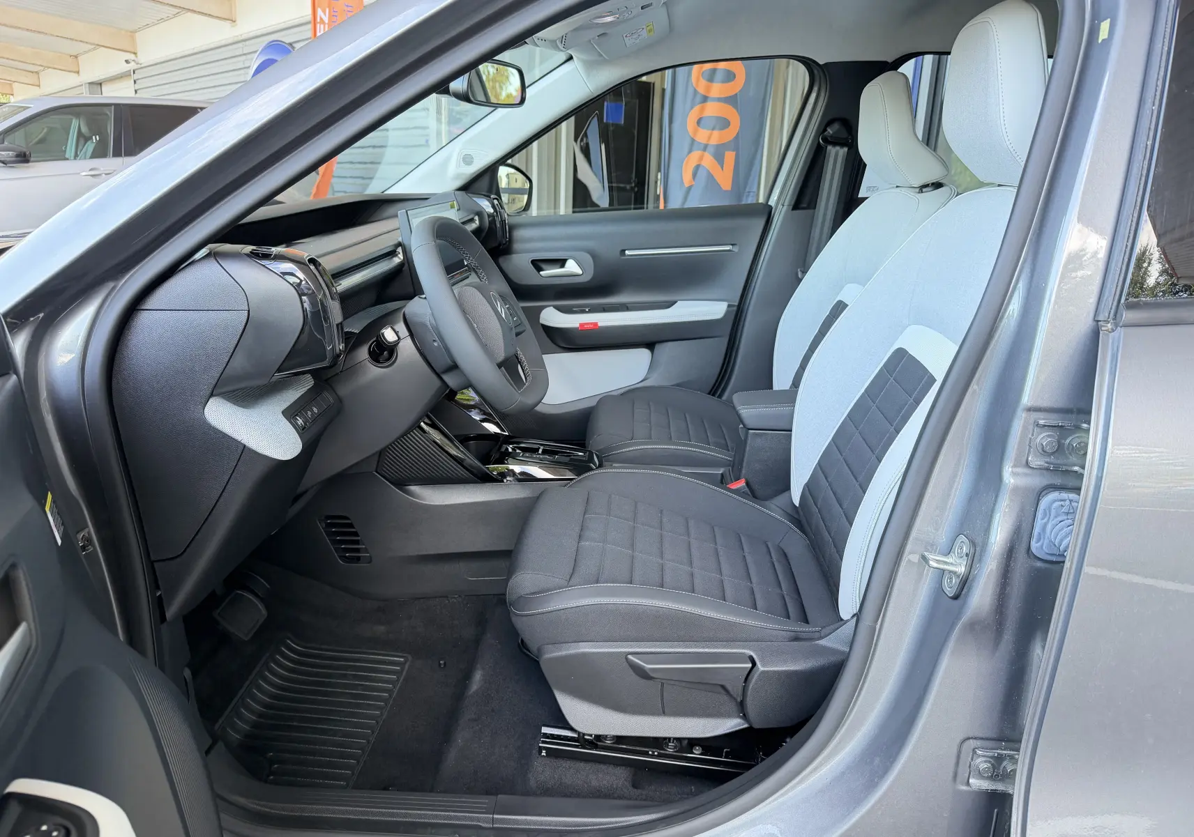 Vue intérieure côté gauche de la CITROEN E-C3 113 MAX 2025 gris Mercury, sièges tissu noir et clair, tableau de bord moderne.