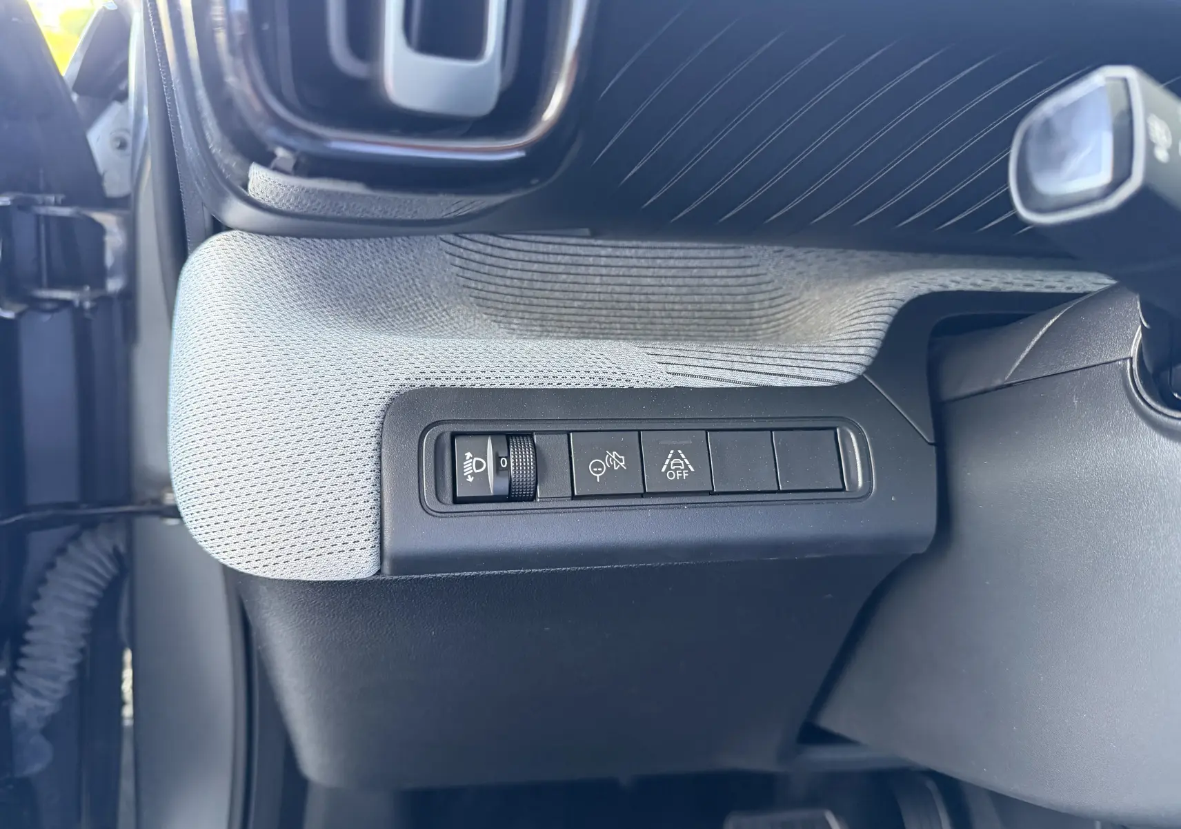 Vue intérieure du tableau de bord côté gauche de la Citroën C3 E-C3 113 MAX 2025 avec sellerie tissu clair et commandes d'éclairage.