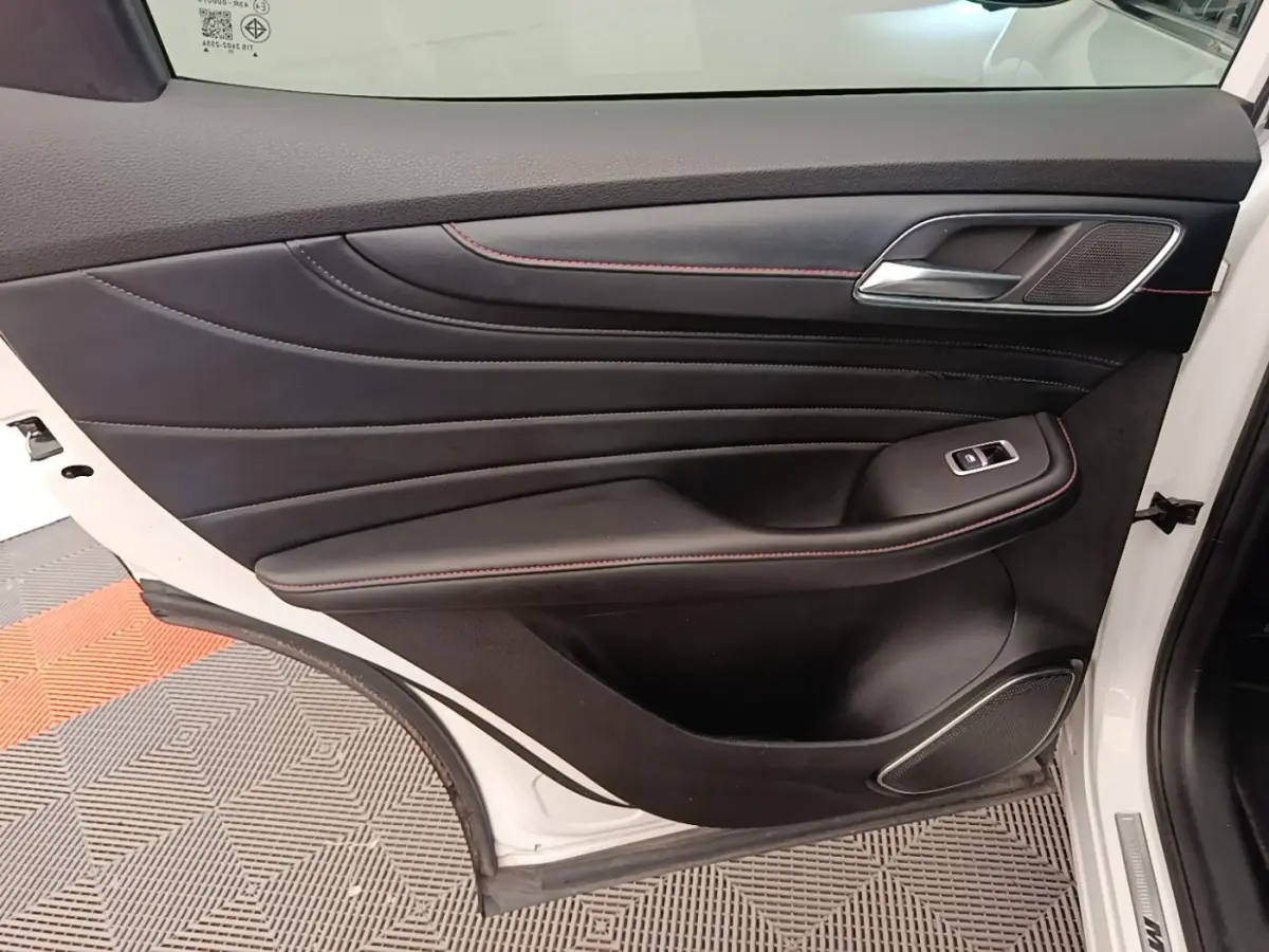Vue intérieure côté gauche de la porte avant blanche du MG Motor EHS 2023 avec garniture noire et surpiqûres rouges.