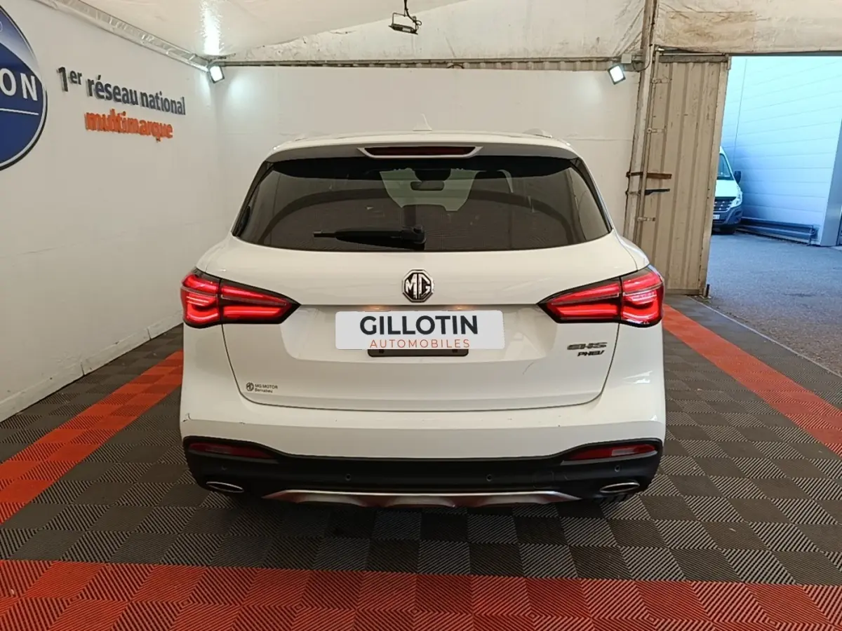 Vue arrière d’un MG Motor EHS blanc 2023 avec feux LED allumés dans un garage intérieur.