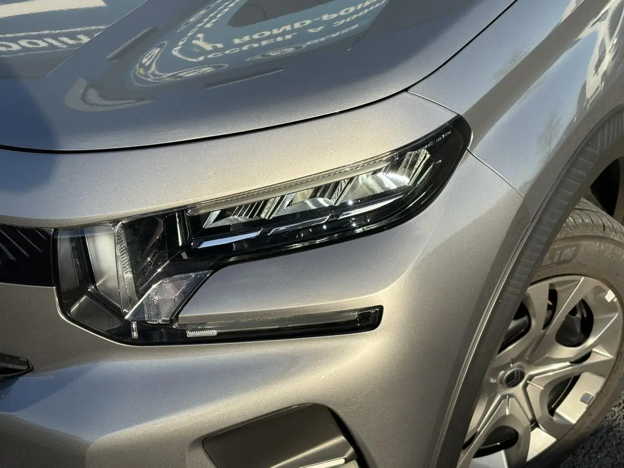 Gros plan sur le phare avant droit et la roue d’une Citroën C3 2025 gris Mercury avec toit noir.