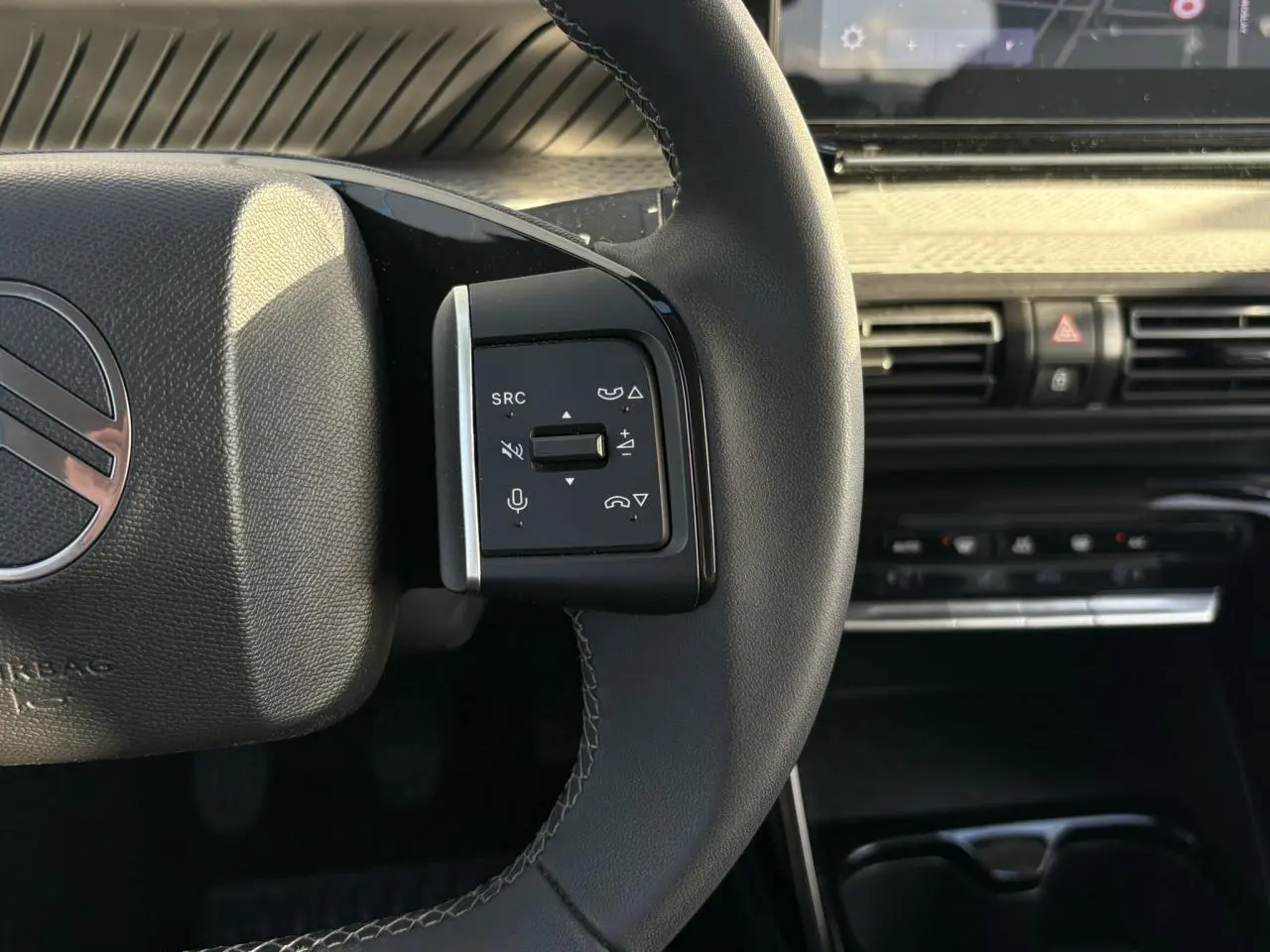 Gros plan sur la commande gauche du volant noir de la Citroën C3 2025 avec tableau de bord et écran tactile en arrière-plan.