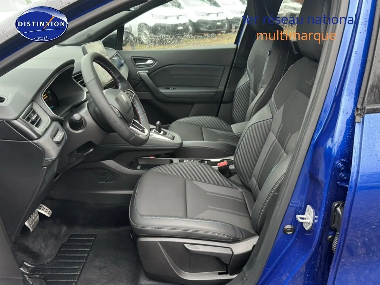 Vue intérieure côté conducteur du Renault Captur 2025 bleu iron, sièges sport noirs avec surpiqûres bleues et volant cuir multifonction.