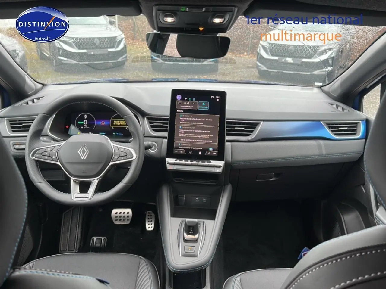 Vue intérieure avant du Renault Captur 2025 hybride, volant cuir, écran tactile vertical et finitions bleu iron t/noir.