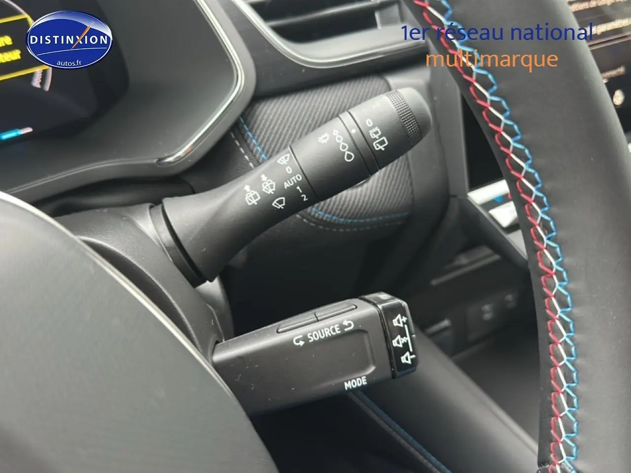 Gros plan sur la commande de phares et volant cuir noir avec surpiqûres tricolores dans l’habitacle du Renault Captur hybride.