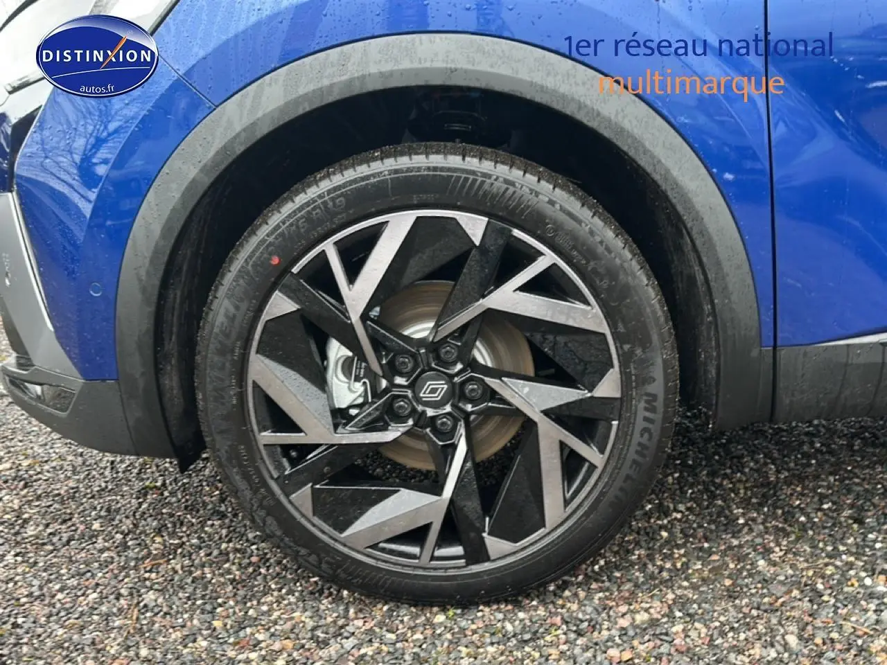 Gros plan sur la roue avant droite du Renault Captur bleu iron avec jante alu noire et argentée au design géométrique.