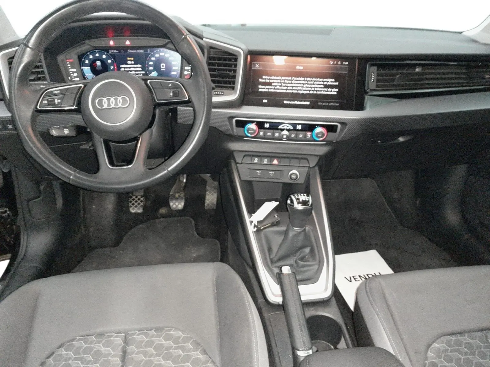 Vue rapprochée de l'écran tactile central de l'Audi A1 Sportback 2023, avec interface multimédia et commandes climatisation visibles.