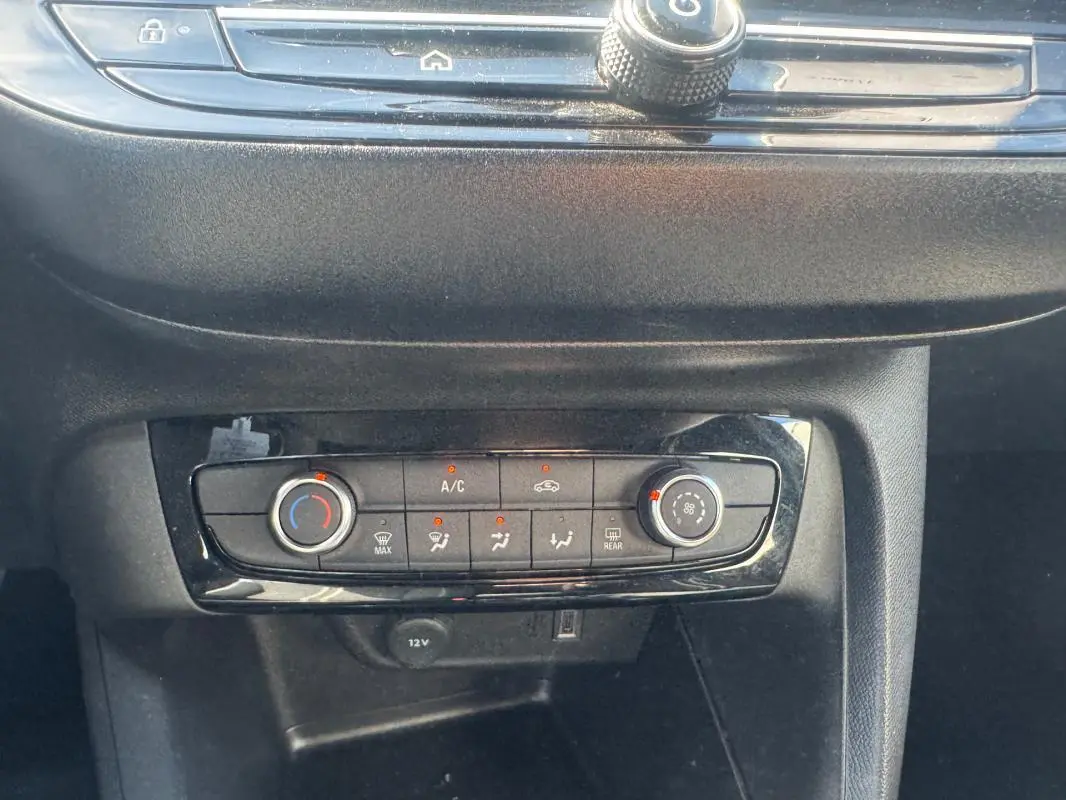 Vue rapprochée de la console centrale de l’Opel Corsa noire, montrant les commandes de climatisation manuelle et prises 12V et USB.