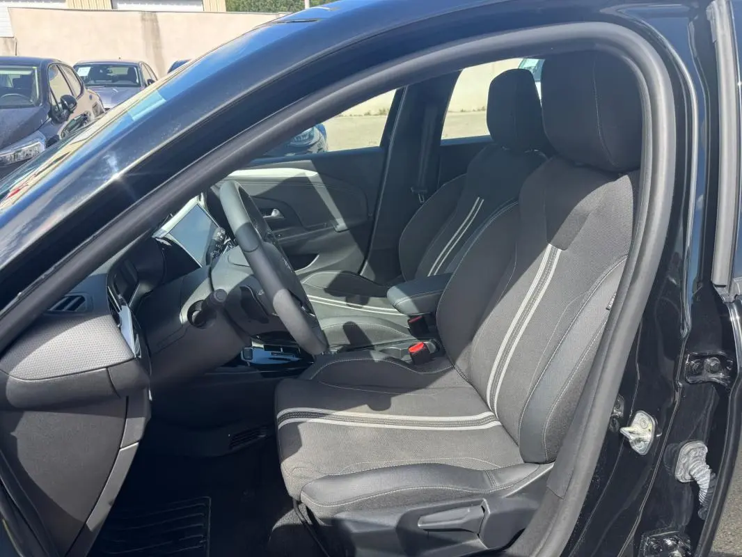 Vue intérieure côté conducteur d'une Opel Corsa noire 2025, sièges tissu avec bandes blanches et accoudoir central.