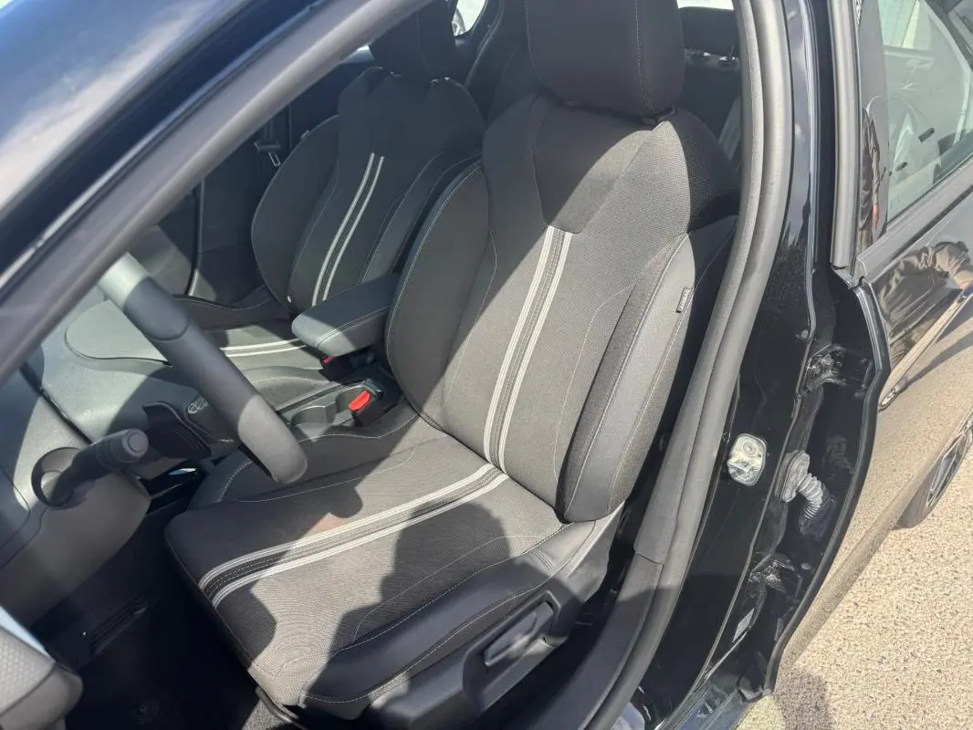 Vue intérieure côté conducteur d'une Opel Corsa noire 2025, sièges tissu noir avec bandes grises et accoudoir central.