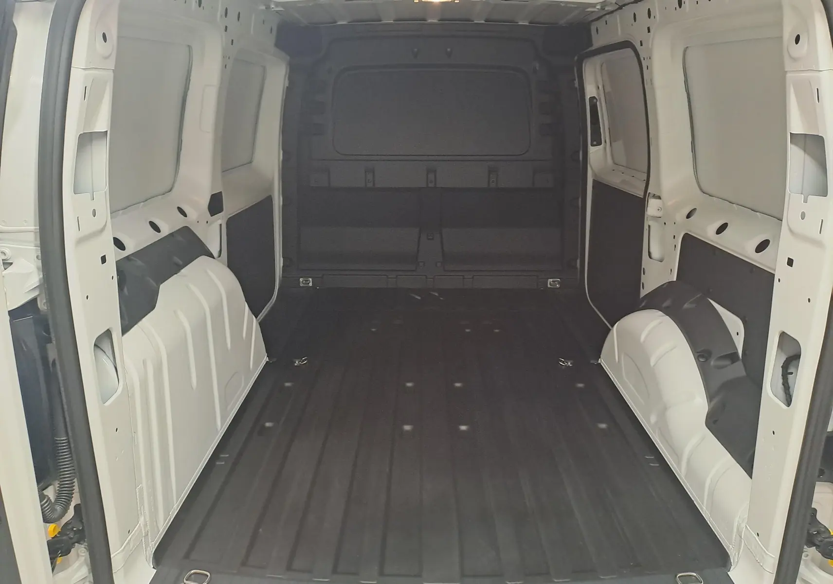 Vue intérieure arrière du Volkswagen Caddy Cargo Maxi blanc candy, montrant l'espace de chargement vide et les parois métalliques.