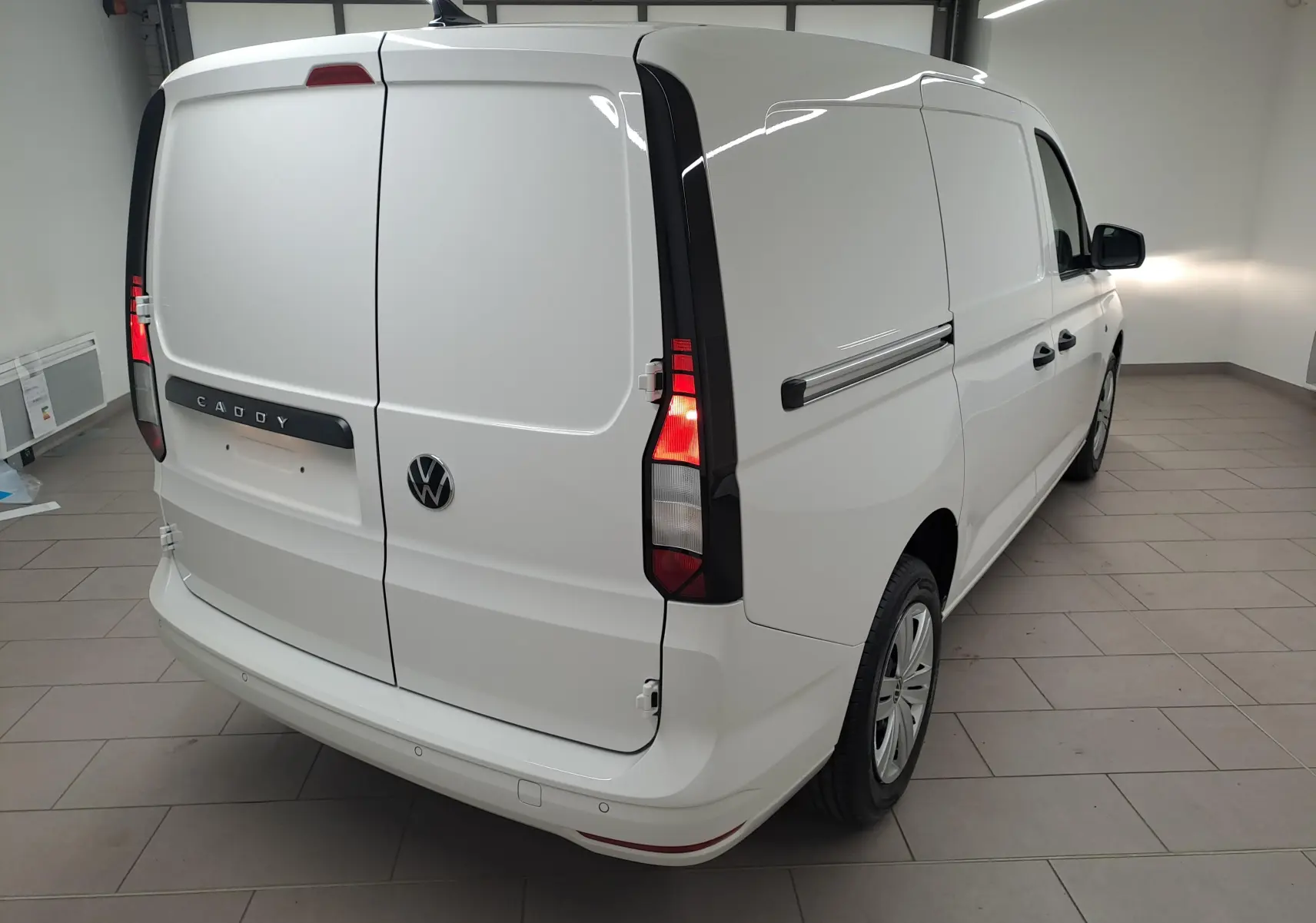 Vue 3/4 arrière droite d’un Volkswagen Caddy Cargo Maxi blanc Candy avec feux arrière allumés dans un intérieur.