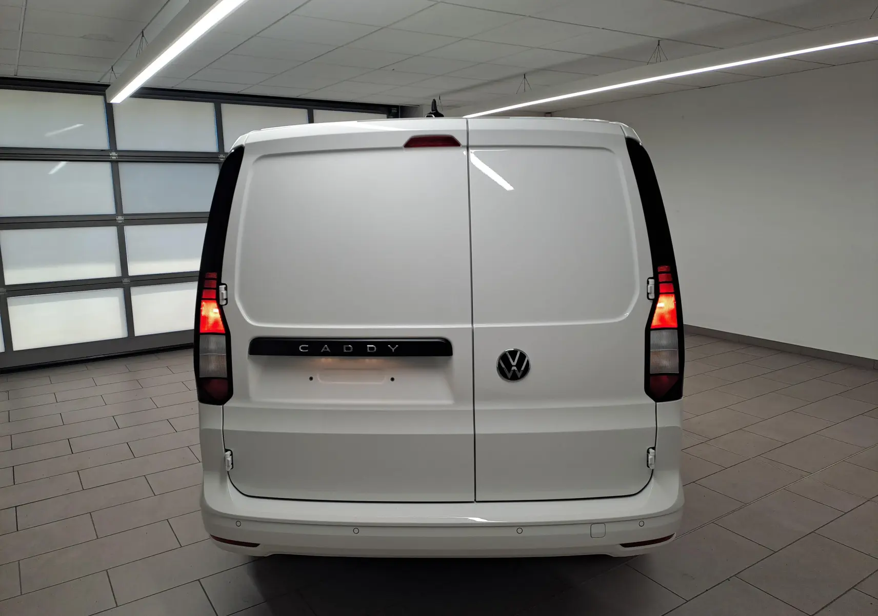 Vue arrière du Volkswagen Caddy Cargo Maxi blanc candy avec feux allumés dans un garage intérieur.