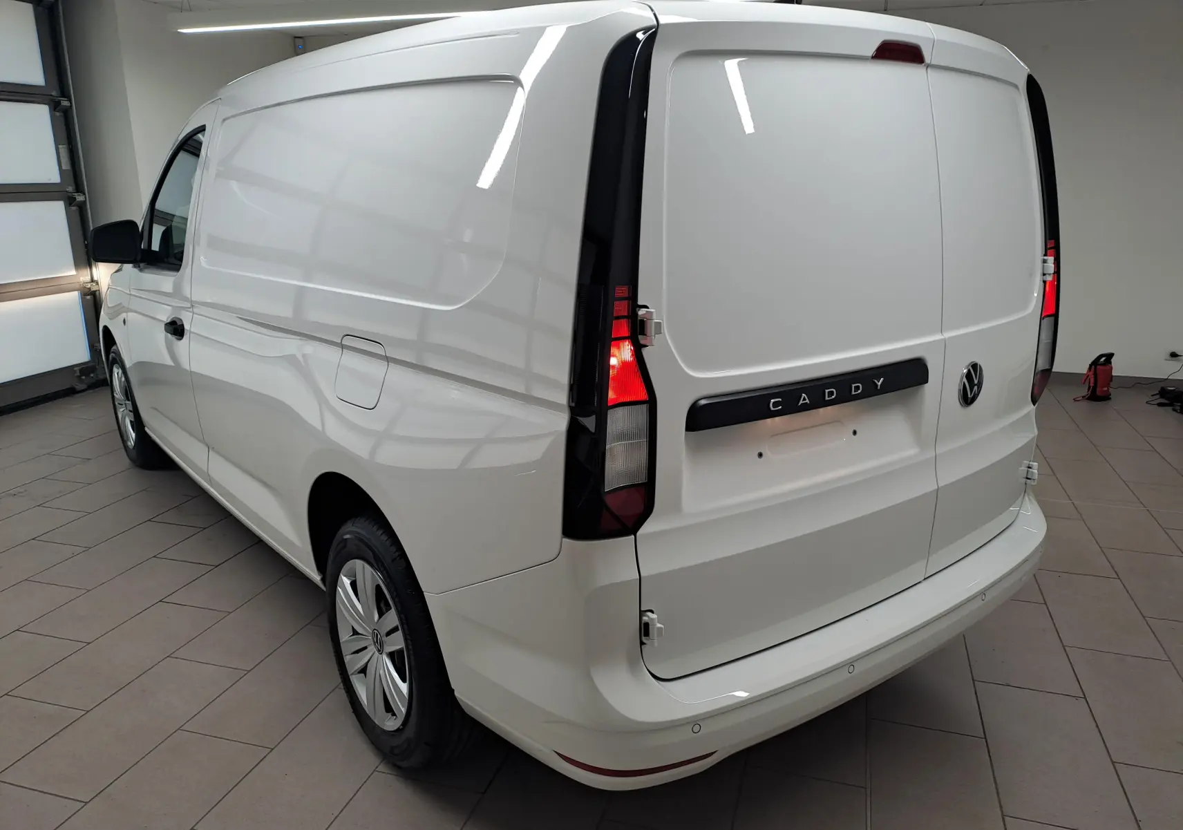 Vue 3/4 arrière droite d’un Volkswagen Caddy Cargo Maxi blanc Candy avec feux arrière allumés en intérieur.