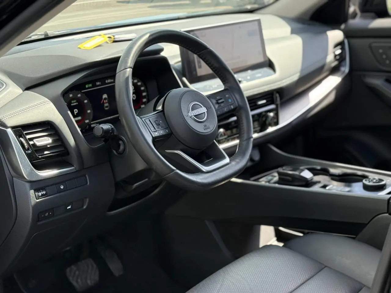 Vue intérieure côté conducteur du Nissan X-TRAIL 2024, volant cuir noir et tableau de bord digital avec écran tactile.