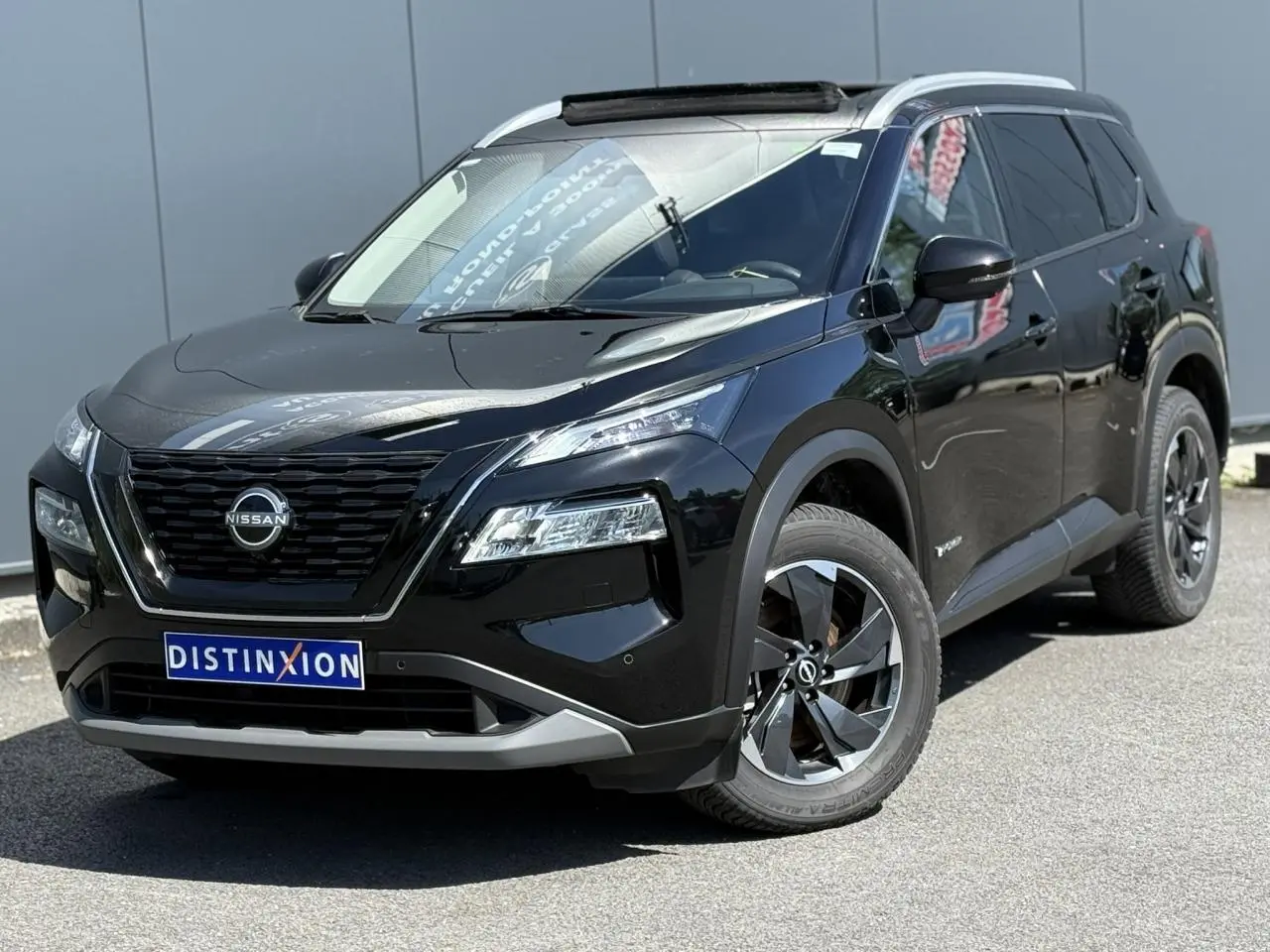 Nissan X-Trail 2024 noir intense en 3/4 avant droit, avec toit panoramique et jantes alliage noires.