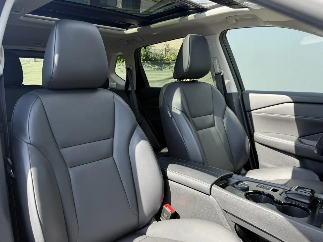 Intérieur Nissan X-TRAIL 2024 vu côté droit, sièges cuir noirs et toit panoramique en verre ouvert.
