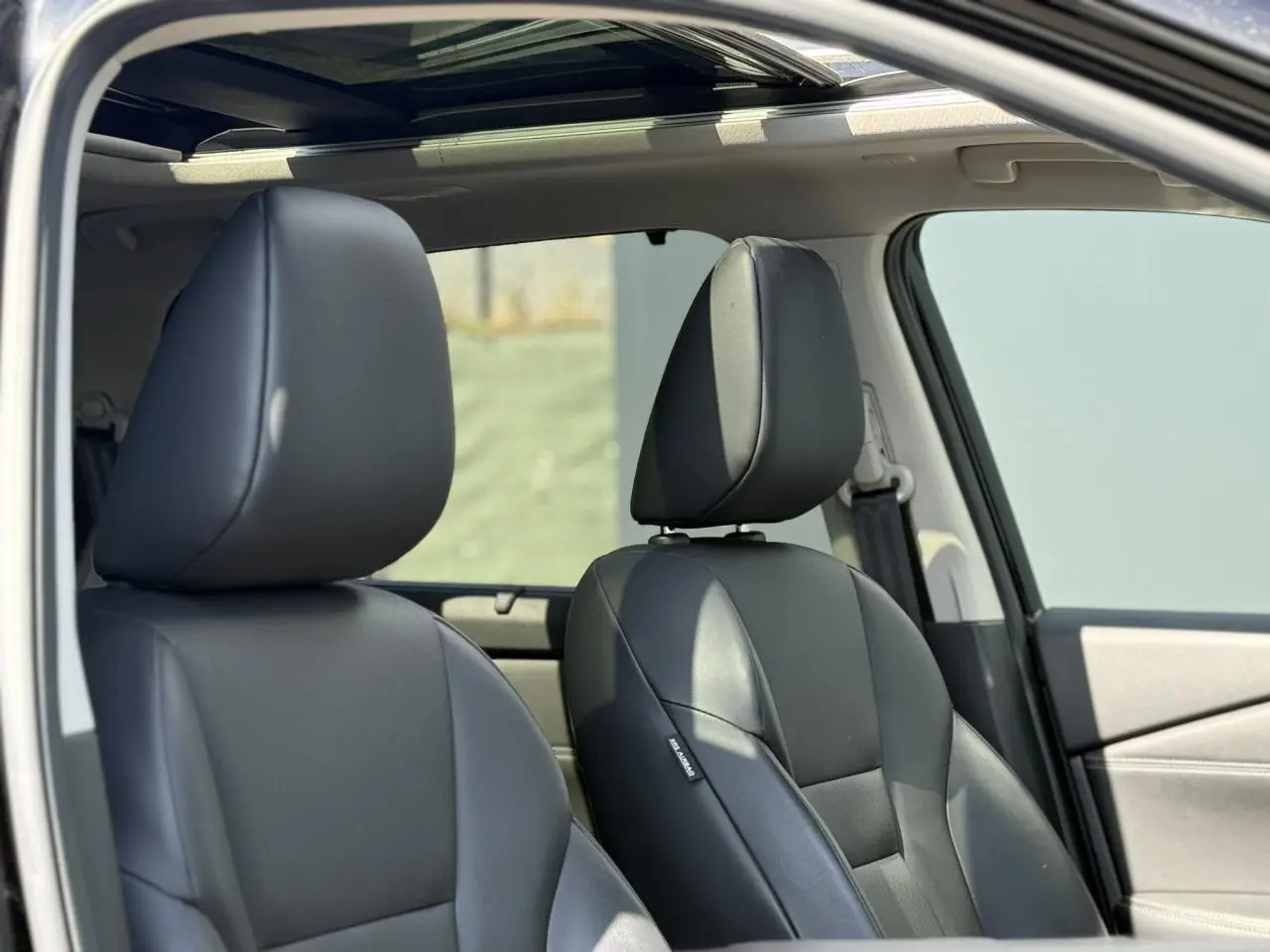 Gros plan sur les sièges avant en cuir noir du Nissan X-TRAIL 2024 avec toit panoramique visible depuis la portière ouverte.